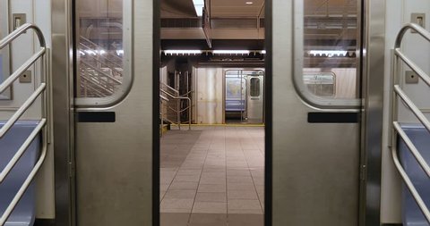 An interior view of the doors on a New York City subway car as they open at an empty platform.  No passengers, perhaps during a pandemic like COVID-19 or Coronavirus.	