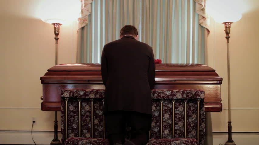 Man kneeling and praying at coffin, funeral service