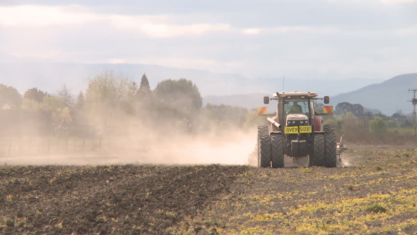A large tractor and implement busy cultivating a dry field 