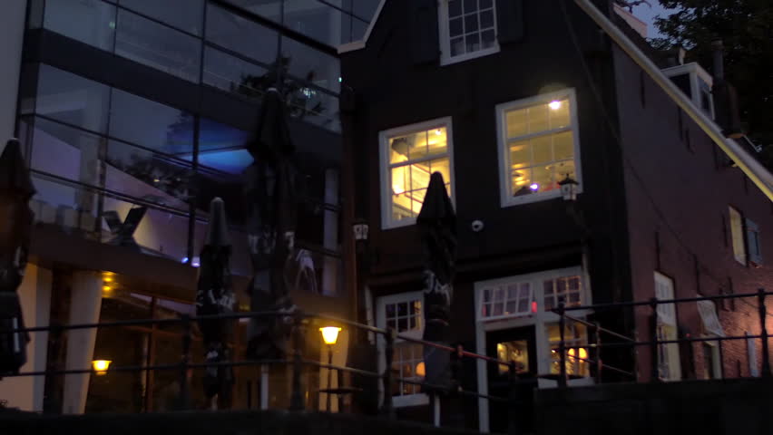 View from moving on the river boat of the buildings with lighting windows on the waterfront, Amsterdam, Netherlands