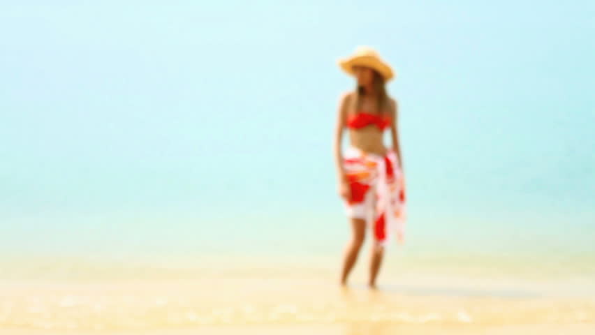 Woman in red bikini walking at tropical beach in sunshine

