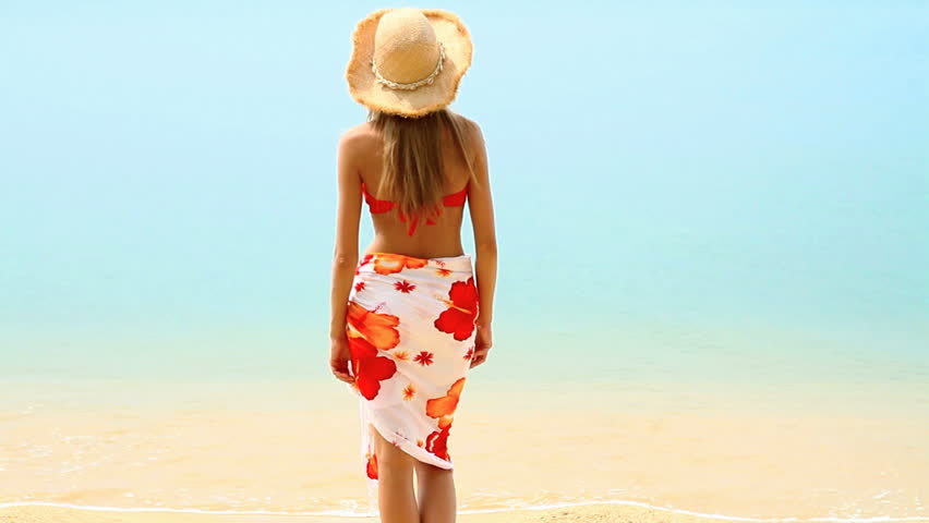 Woman wearing pareo and bikini, standing at tropical beach
