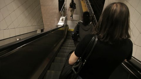going down a subway escalator behind commuters who step onto the platform