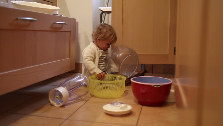 Baby playing with kitchen utilities. Toddler at play at the kitchen with pots and pans