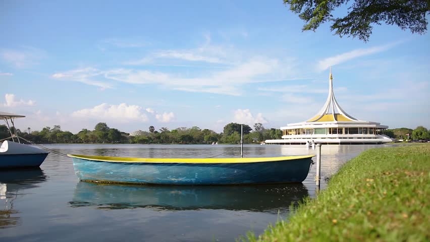The tranquil lake with a boat in the foreground and the Ratchamangkala Pavilion of Suan Luang Rama IX Public Park Bangkok in a background at afternoon.