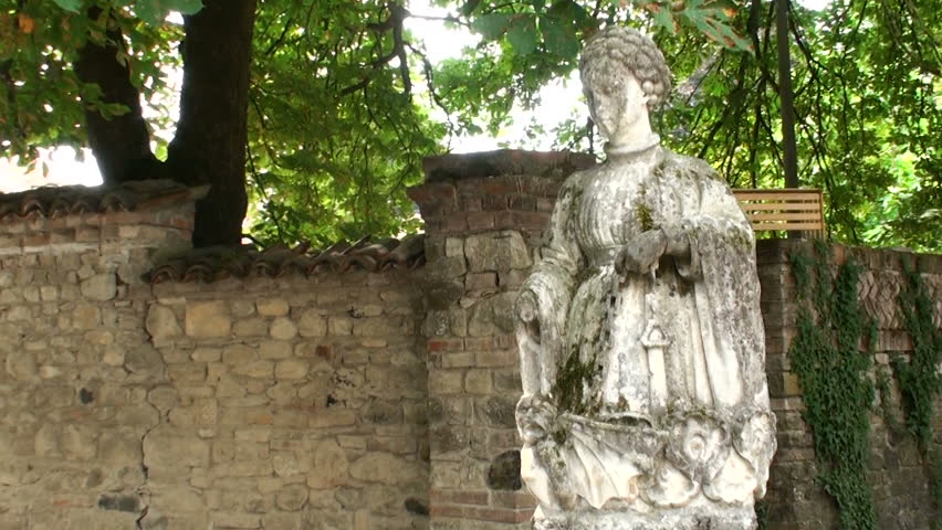Statue of a young medieval woman with the iron chain in hand, dressed in a gown. One of the damaged sculptures with broken hand stored in a small Italian medieval village