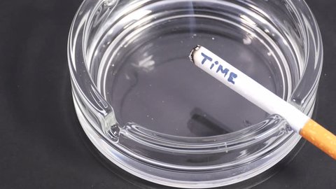A cigarette with an inscription TIME smolders in a transparent ashtray.