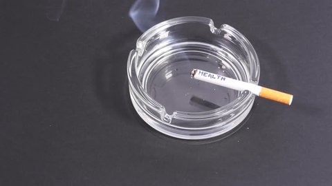 Cigarette with an inscription 'Health' burns in the ashtray. 