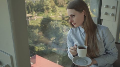 Concept: millennial, connections, lifestyle. Business casual dressed attractive girl drink tea by the window of trendy restaurant in skyscraper. HD 1080p.