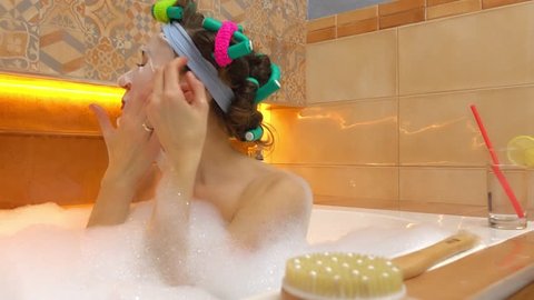 Brunette woman using face mask in foamy bath. Beauty treatments at home. 4K video