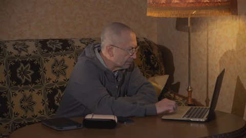 Grandpa sitting at a desk and working at a laptop. Is typing.