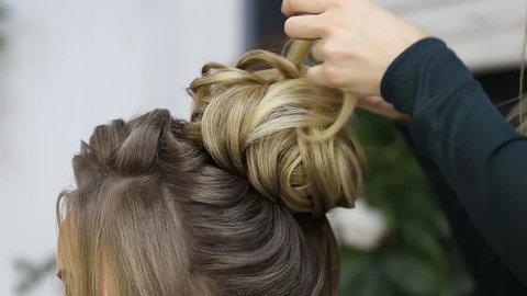 Hairdresser creating complicated evening and wedding hairstyles at barbershop salon. Close-up of hands corrects hair curls and strands