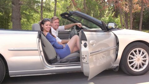 Young couple sit in cabriolet and girl closes door at sunny summer day