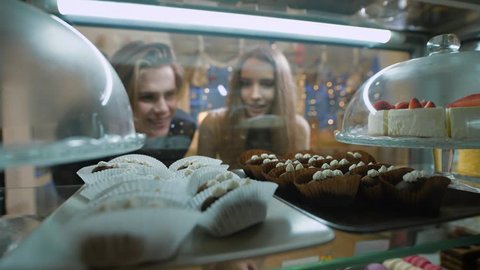 Beautiful couple of young people in a candy store. The girl and the guy chosen Cake and desserts for themselves. Showcase pleasantly decorated