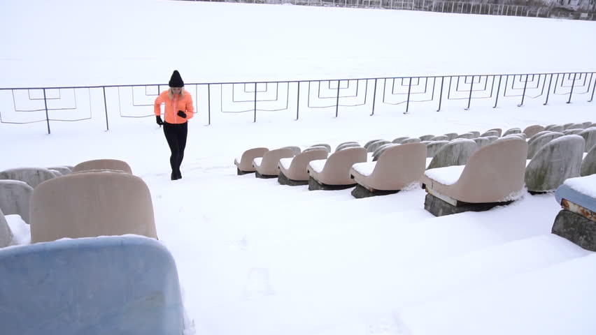  Fitness woman jogging in snowy stadium.  Jogging up stairs covered with snow. Outdoor workout on a cold winter day. Young sportswoman running. Slow motion camera 120 fps