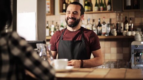 small business, people and service concept - happy man or waiter with cup serving customer and taking money payment at coffee shop
