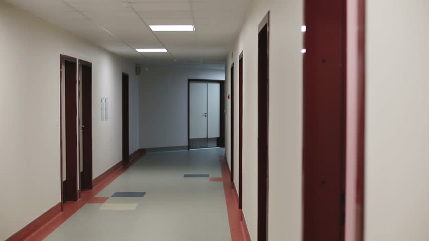 Beautiful couple walking in the hall the hospital. Young man with glasses and a beautiful girl in a black dress goes a long corridor holding hands.