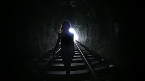 Mysterious woman walking in dark tunnel. Female silhouette on background of light at end of corridor. Person go alone in darkness. Death and afterlife concept. Urban subway with long tunnel - Powered by Shutterstock - Get 15% off with code: PIKWIZARD15