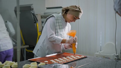 Some pastry chefs at work in a candy shop. One of the women involved in the creation of pasta. Using a pastry bagshe pushes the circles on a table
