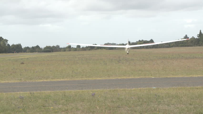 A glider lands on a grass runway