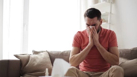 healthcare, flu, hygiene and people concept - sick man blowing nose to paper napkin at home