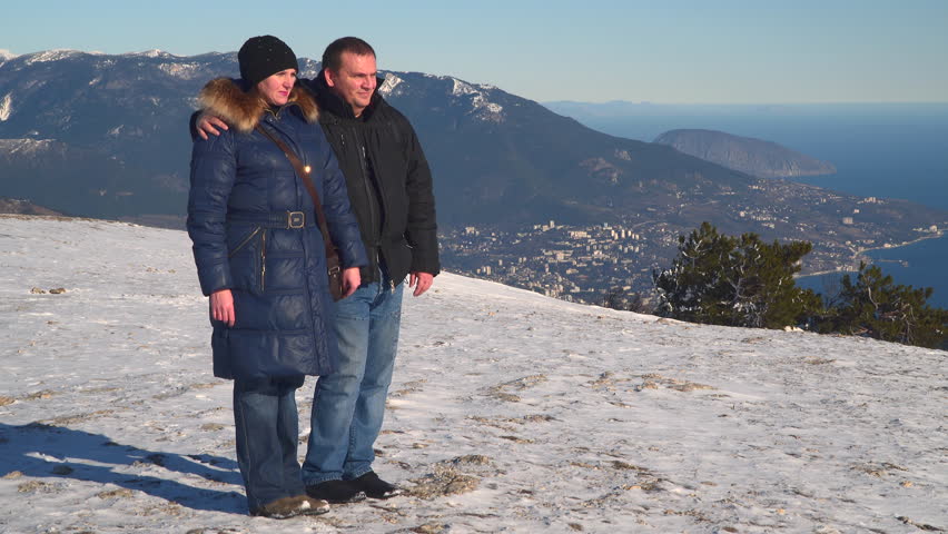 Woman and man standing on the snow-covered plateau. Below can be seen the city and the sea