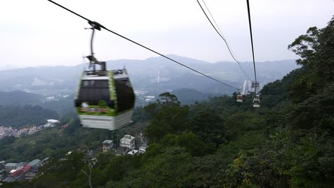 Aerial view from gondola lift slide move down, evening time, mountains landscape, Wenshan District. Natural woodland hills and some urban area in ravine. Long shot in dusk, foresty hill side at right