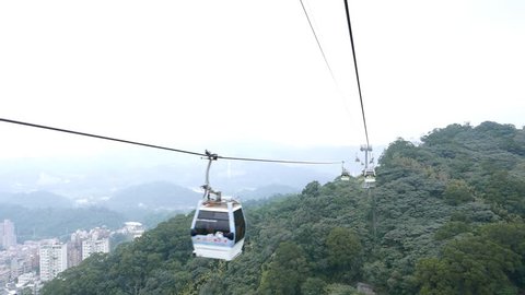 TAIPEI, TAIWAN - FEBRUARY 17, 2015: Aerial perspective from gondola lift, mountain landscape in dusk. POV slide down by Maokong air lift system, small cabin hang on steel cable, move towards and pass