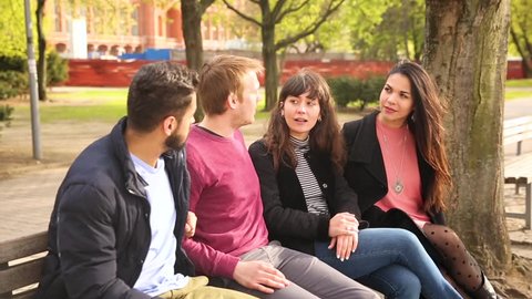 Group of friends having fun at park in Berlin. Mixed race group with caucasian, middle eastern and nordic persons, sitting on a bench and talking. Happiness and friendship concepts.