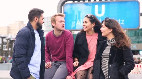 Group of friends having fun together in Berlin. They are a mixed race group with caucasian, middle eastern and nordic people. On background there is an Alexanderplatz underground station sign.