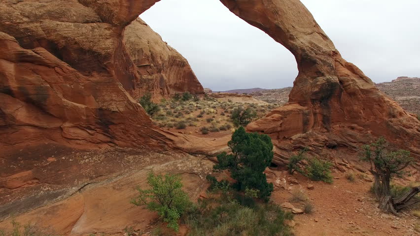 Drone flying through arch to view valley below on a cloudy day, in Moab, Utah.