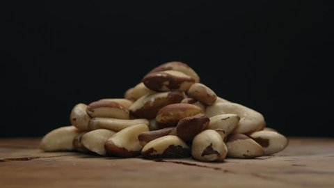 Pile of brazil nuts on a wooden table isolated on black, rotating 