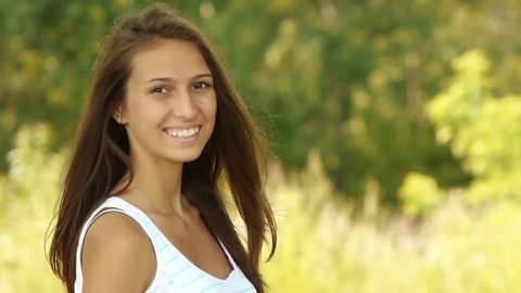 Portrait of beautiful smiling young woman with camera, against green of summer park.