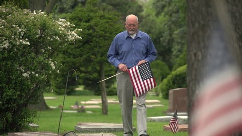 Older man walking through cemetery holding US flag
