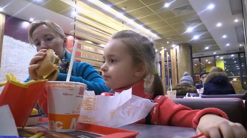 Little girl and mom eating hamburger, fries potato and drink cola in eatery fastfood McDonald's. Moscow - 2017.