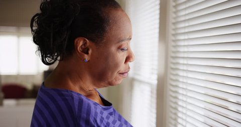 An older black woman mournfully looks out her window. An elderly African American woman sadly looks out her window. 4k