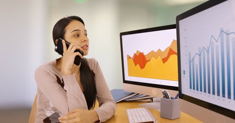 A young businesswoman talks on her mobile phone referencing the graphs. A young woman talks on her smart phone about business. 4k