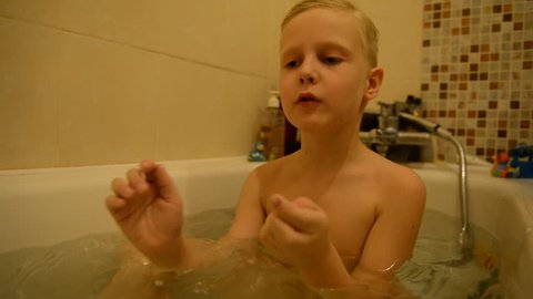 The child bathes in a bathroom with water, foam. blond boy 