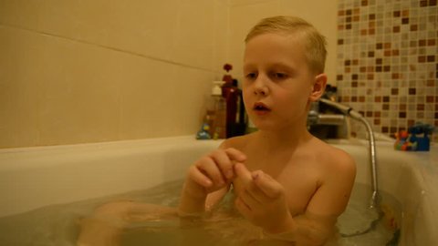 The child bathes in a bathroom with water, foam. blond boy 