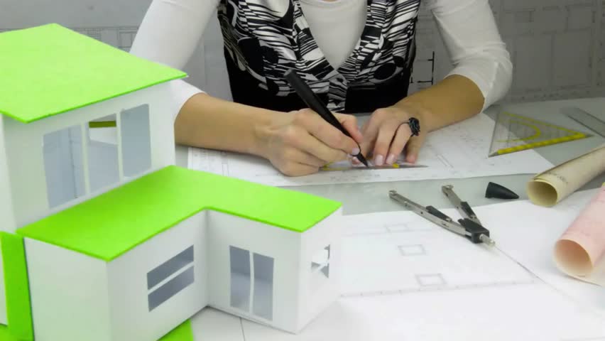 Woman architect at work. 
Architect at work drawing a plan for a new house. A model of the house in the forefront, plans on the table. Classical architect. Royalty-Free Stock Footage #22780552