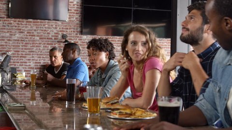 Group Of Friends Watching Game In Sports Bar On Screens