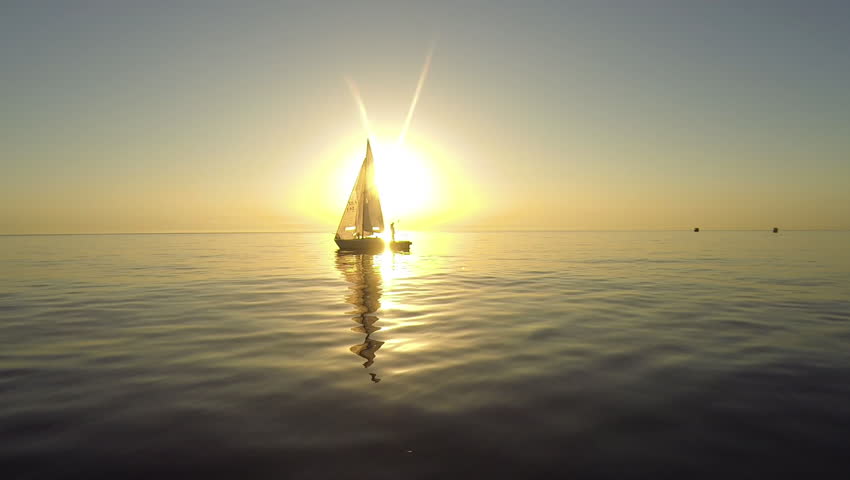 Sailing boat at sunrise with gold sun in background
Drone on sailboat at sunrise