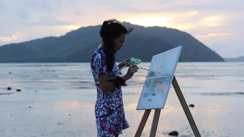 young girl draws a sunrise, on the beach at low tide. Work on the painting.
