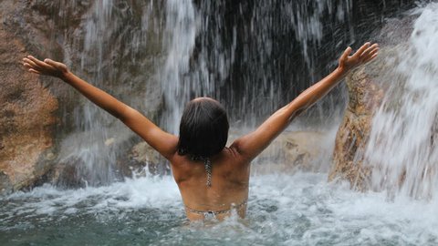 young woman open arms to amazing waterfall expressing happiness and freedom in slow motion in beautiful nature.