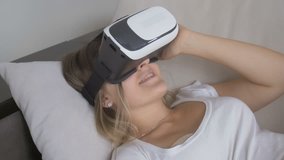 Closeup of happy smiling woman lying on sofa and using VR headset. Footage in 4K resolution