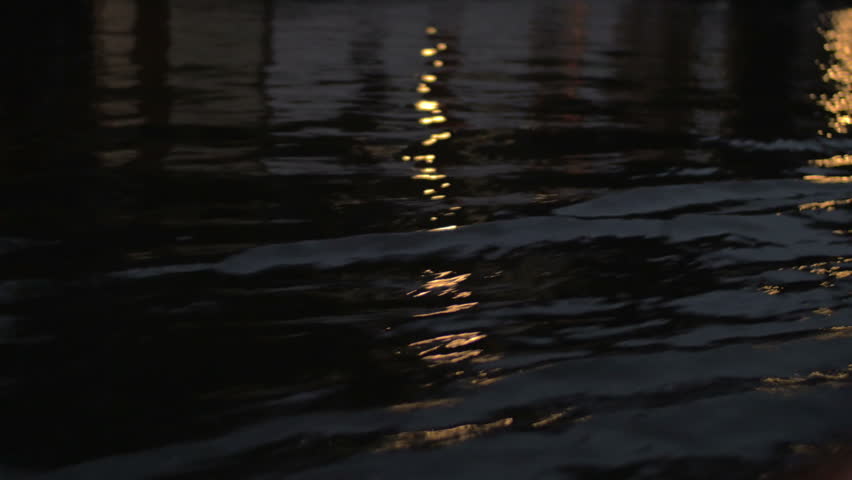 Close up view of river wave on moving boat at night, then buildings, cars on the waterfront, Amsterdam, Netherlands