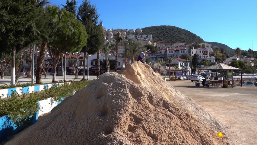4K Zoom in boy siting on big sand pile and scattering sand
