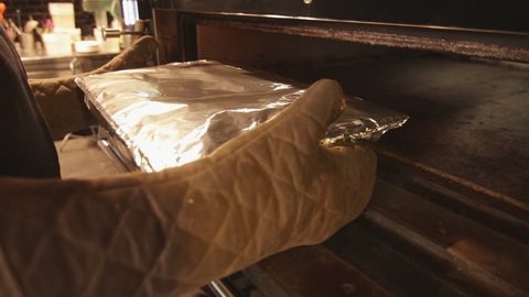 Taking hot tray covered in aluminium paper out of an industrial oven
