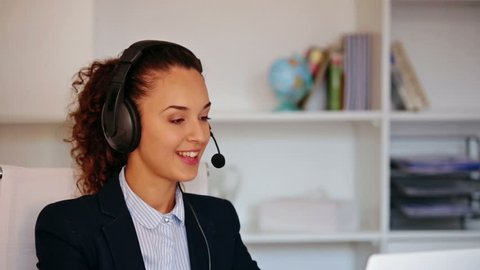 Cheerful girl with headset and laptop answering call in office