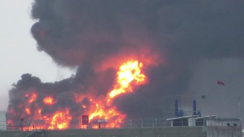 Huge fire blaze from burning oil container in refinery. Firefighter water jet extinguish the fire started near a petrol storage tank. Black rain, acid rain, smog, smoke, ash, ecological pollution